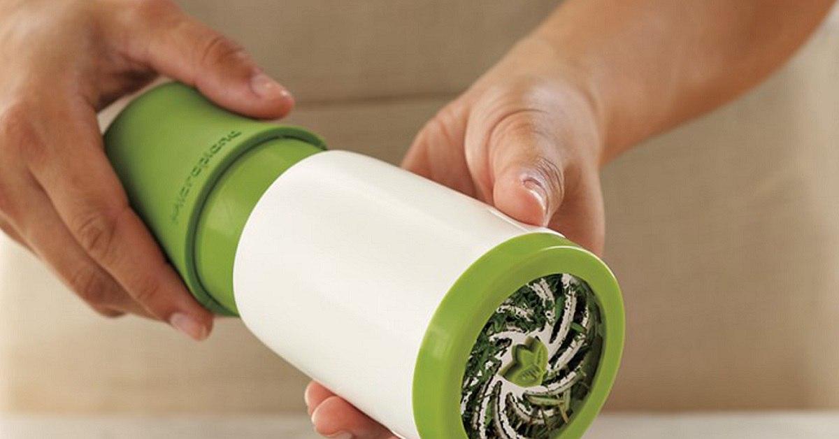  A person's hand holding a green and white kitchen gadget that minces herbs.